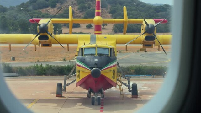 Italian canadair cl-415 amphibious aircraft seen through an airplane window. The yellow firefighter water bomber is parked on the tarmac