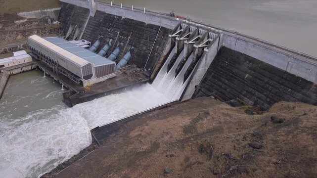 Rising view of Clyde Dam with all four floodgates open, showcasing renewable hydroelectric power, major engineering and sustainable energy infrastructure beside Lake Dunstan.