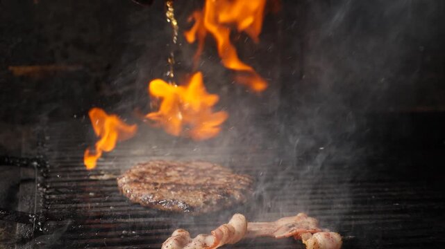 Juicy beef patty and chicken pieces grilling on metal grate with intense orange flames and thick white smoke rising. Chef pouring oil from above, dramatic restaurant kitchen cooking process Slow motio
