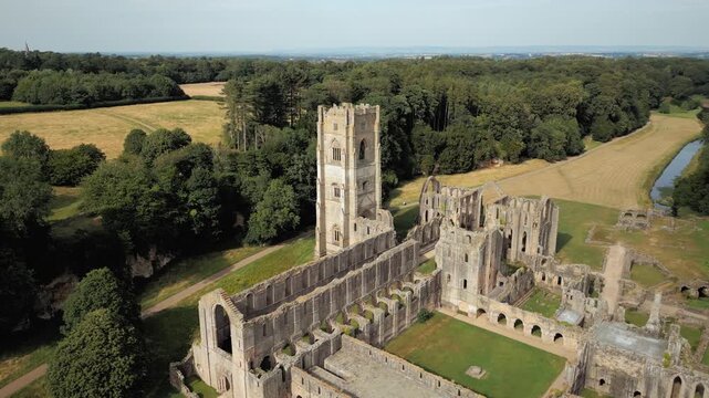 Ancient stone ruins stand tall amid green fields. Towering arches frame the historic site. Fountains Abby, World Heritage Site near Harrogate North Yorkshire UK,
