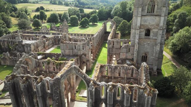 Ancient abbey stands tall amidst green hills. Stone arches frame a quiet, sunlit courtyard. Fountains Abby, World Heritage Site near Harrogate North Yorkshire UK,