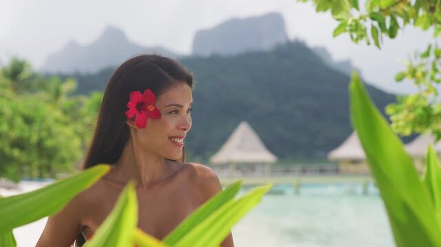 Beach beauty woman natural girl looking serene on tropical beach. Asian bikini model wearing hibicus flower body care wellness and spa pampering. Raw video of real woman model without makeup