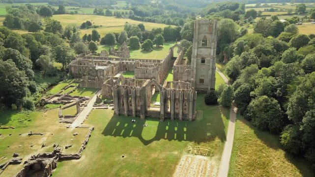 Ancient stones stand tall, surrounded by lush greenery. Sunlight dances across weathered walls and open courtyards. Fountains Abby, World Heritage Site near Harrogate North Yorkshire UK,
