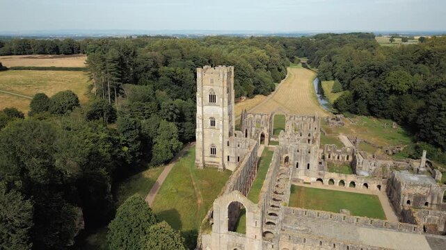 Ancient ruins stand tall amid green fields and trees. Aerial view reveals grand architecture lost to time. Fountains Abby, World Heritage Site near Harrogate North Yorkshire UK,