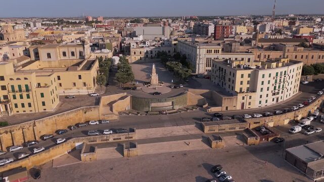Aerial shot flying towards the Fontana dell Impero and Monumento ai Caduti surrounded by historic architecture in Apulia.
