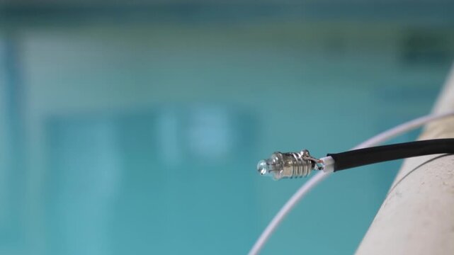 Close up of a small light bulb on a homemade wire with a pool in the background