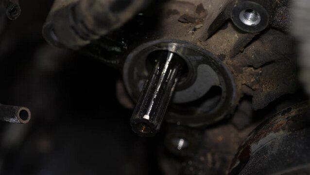 A close-up view shows an exposed splined shaft extending from a greasy and dirty automotive component during engine maintenance.