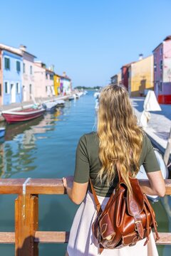 Young woman in front of colorful houses, canal with boats and colorful house facades, Burano Island, Venice, Veneto, Italy