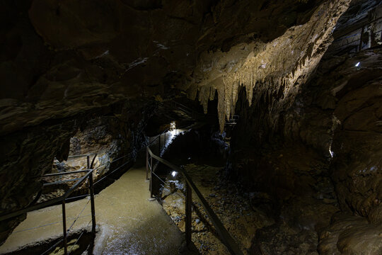 Tourist walkway with safety railings leading past stalactites hanging from the rock ceiling inside a passage of the Lurgrotte Peggau cave system in Styria, Austria
