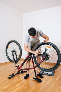 Wide vertical shot of focused mechanic performing bicycle maintenance at home. Servicing, cleaning drivetrain with lubricant. Hobby and active lifestyle concept. Minimalist interior with copy space.