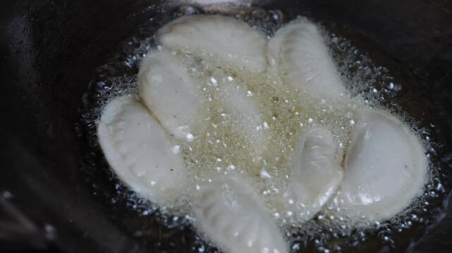 Close up of dumplings frying in hot oil in a pan, with bubbling oil and a crisp cooking texture