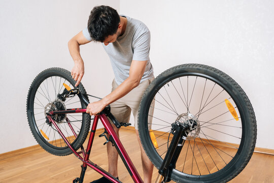 Focused cyclist performing maintenance on bicycle in living room. Man fixing gear system on bike mounted on workstand. Hobby, diy, active lifestyle concept with copy space on wall.