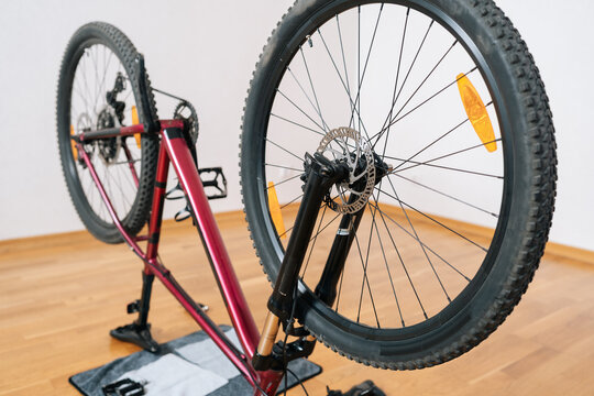 Mountain bike standing upside down on seat. Concept of disc brake system and wheels, undergoing maintenance and repair work indoors on wooden floor, close-up, cropped shot, nobody, no people.