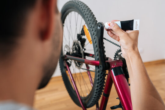 Person hands applying grease from tube onto pedal arm and crankset of bicycle during routine maintenance, ensuring smooth operation and prolonging bike lifespan for safe cycling.