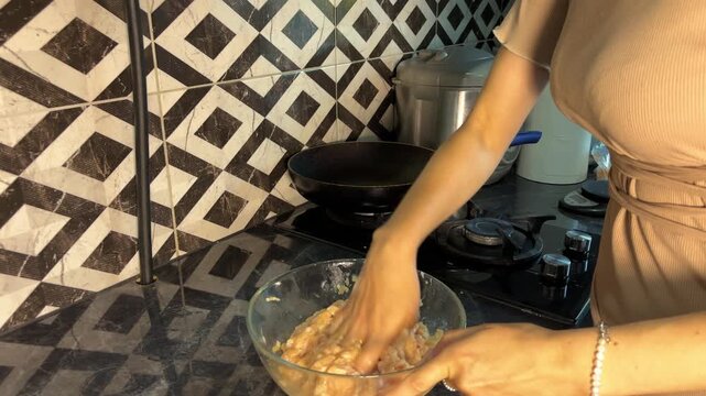 Hands knead seasoned ground chicken mixture in a clear bowl before frying.
