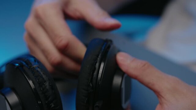 Closeup cropped shot of hands peeling off old, worn, flaking faux leather from headphone ear pads. Concept of DIY repair, maintenance, product obsolescence, upcycling electronic devices.