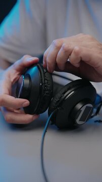Man hands holding old, broken headphones with cracked and peeling leatherette ear pads. Concept of worn out material falling apart from overuse, planned obsolescence and poor quality, slow motion.