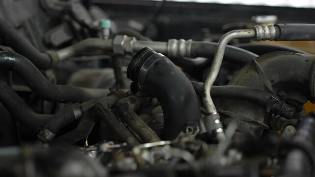 A curved black rubber air intake hose is secured with a clamp amid various pipes and tubes inside a dusty car engine bay.