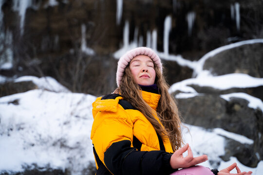 Peaceful woman practicing meditation with mudra gesture in winter nature, mindfulness, wellness, emotional balance and self care concept.
