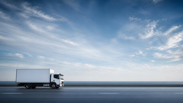White delivery truck driving on a long asphalt road against a vast blue sky with light clouds and a distant ocean horizon line in the background