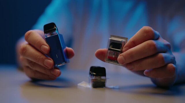 Man holding blue electronic cigarette new refill pod in blister pack. Close-up shot of preparing to change cartridge on modern vaping device. Process of maintaining heated electronic cigarette device.