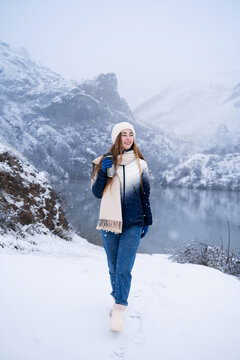 Woman with thermos walking outdoors in winter nature, mountain lake background, travel, warm beverage and lifestyle concept.