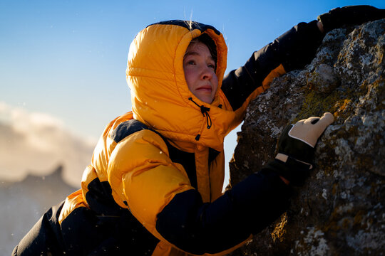 Woman climbing rocky slope in winter mountains, wearing warm winter jacket, mountaineering activity, determination, outdoor adventure and alpine sport concept.