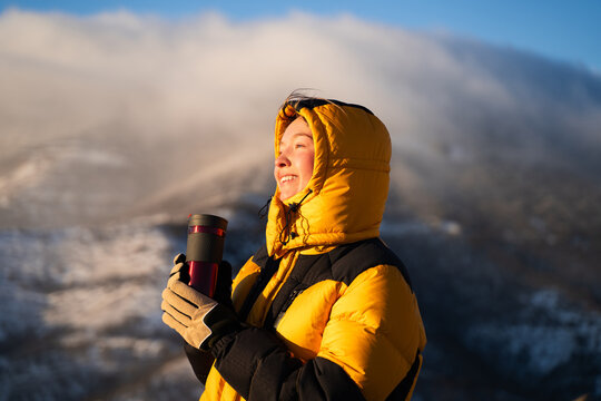 Woman with thermos cup enjoying sunrise in snowy mountains, outdoor active lifestyle, travel and winter recreation concept.