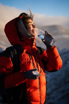 Woman traveler drinking water outdoors at sunrise in snowy mountains, hydration, healthy lifestyle, wellness and travel concept.