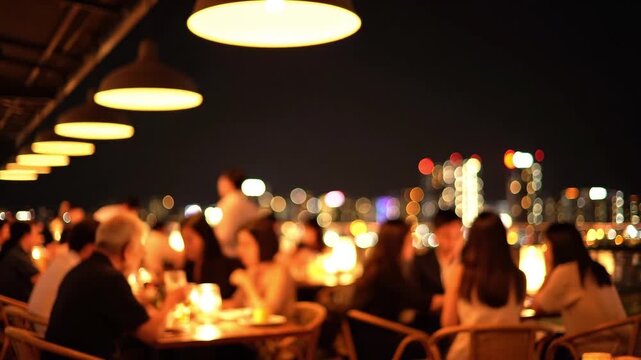 Defocused abstract background of a crowded rooftop restaurant at night, people dining and socializing under warm lamps with beautiful sparkling city skyline bokeh lights