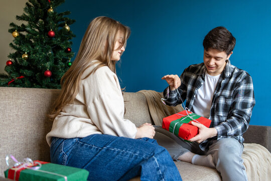 Young couple exchange Christmas gift beside decorated tree