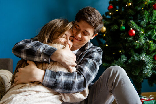 Young couple embrace beside decorated Christmas tree at home