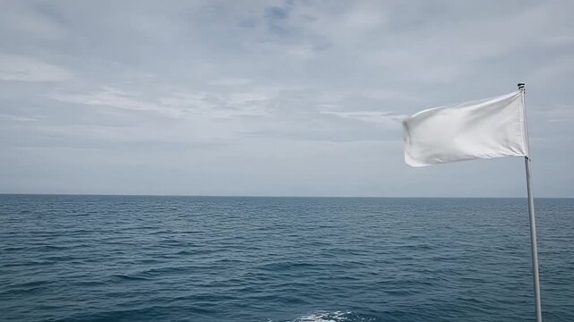 White flag waving on a pole against a vast ocean and cloudy sky