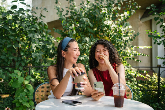 Two students laugh together at an outdoor cafe table