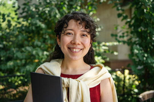 Smiling student holding laptop outdoors on campus