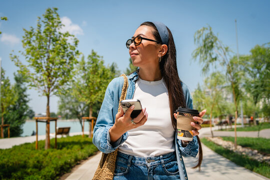Young woman use smartphone and coffee cup in city park