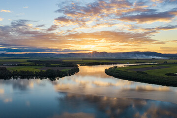Fototapeta premium Aerial view of sunset over the Clarence River and surrounding farmland, with smoke from a fire drifting across the rural landscape beneath a colourful evening sky 