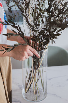 Woman arranging leafy branches in glass vase at home