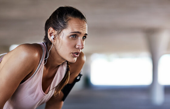 Earphones, girl and tired in parking lot for fitness, catch breath and exercise break with music. Underground, runner or reflection with tech for wellness, workout fatigue or cardio tips in audio