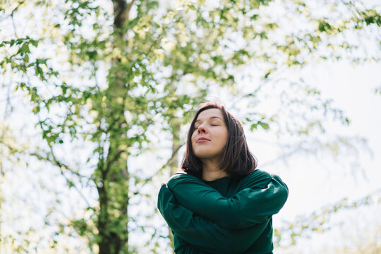 Woman embrace herself peacefully in a sunlit forest
