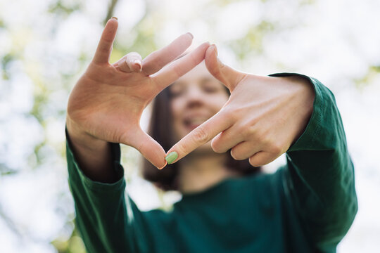 Woman frames nature scene with hands in forest