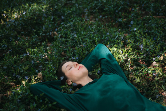 Woman resting peacefully on forest floor in green clothing
