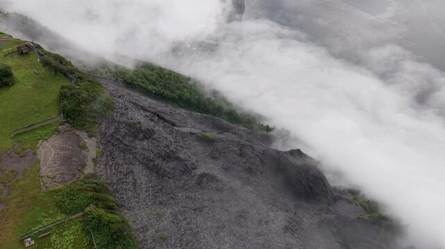 Aerial view of thick cloud blanket rolling over sharp dark rocky mountain ridge in Mont Saint-Pierre Gaspesie Quebec Canada drone footage