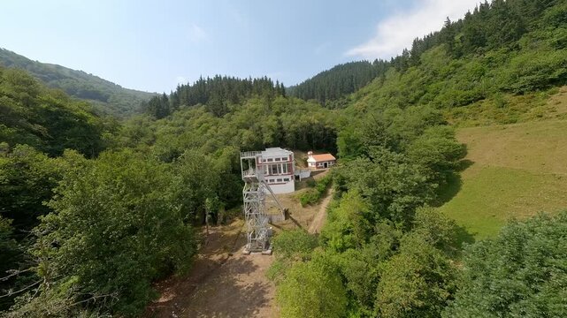 An aerial perspective of the historic Pozo de San Fernando coal mine ruins nestled in the lush green mountains of Aller, Asturias. Showcases industrial heritage and sustainable nature recovery.