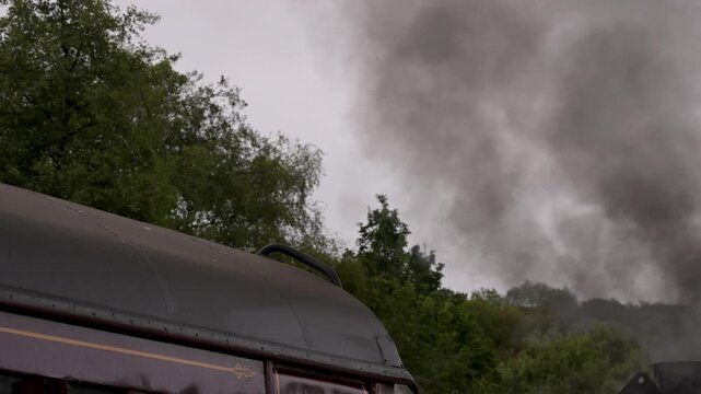 Vintage steam locomotive reverses past the camera at Churnet Valley Railway, with thick smoke rising beside a maroon carriage on an overcast day.