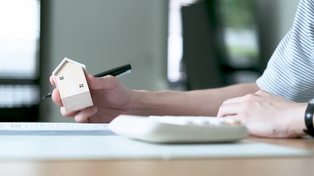 Person reviewing documents and calculating home expenses with a house model, concept of mortgage loan, interest rate, budgeting, real estate purchase and financial planning.
