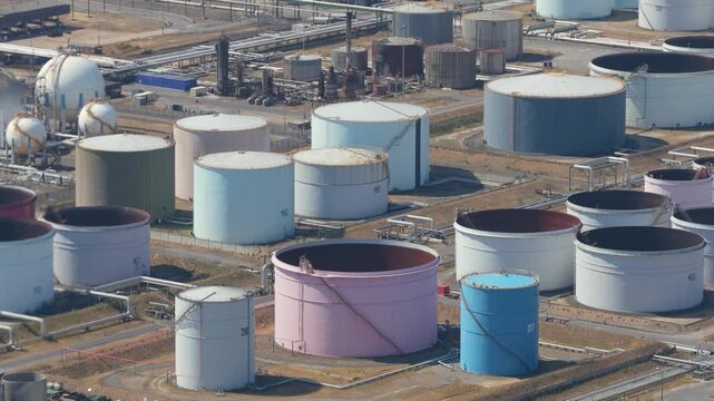 Large cylindrical storage tanks hold crude oil and refined products within this industrial facility on a clear day with metal pipes and structures connecting the various containers for distribution