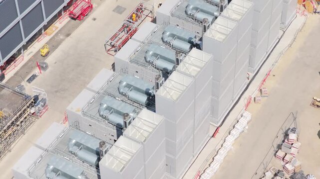 Aerial view showing workers walking near industrial cooling units at a Data Center construction site on a bright sunny afternoon with materials and tools stored around the perimeter of the facility