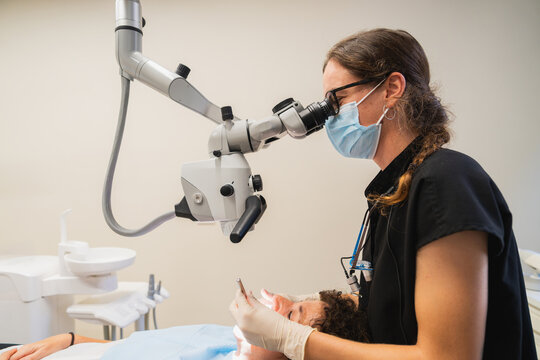 Female dentist using operating microscope performing root canal treatment