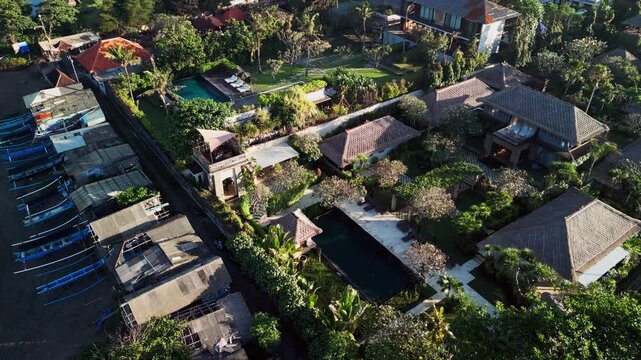 Bali tropical resort villa showcases traditional thatched roof architecture landscaped gardens a private pool and beachside surroundings under warm morning sunlight aerial drone footage